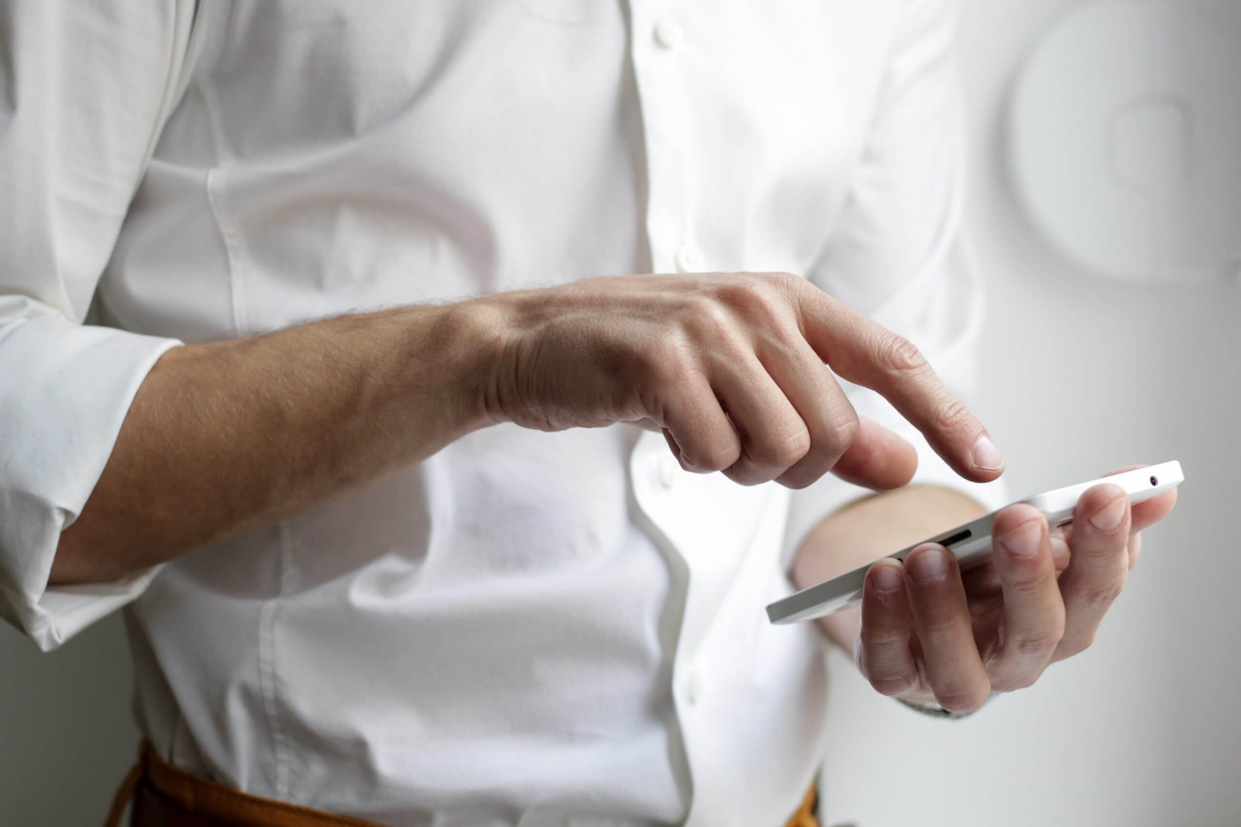 Un homme en chemise blanche tient un téléphone portable dans sa main.